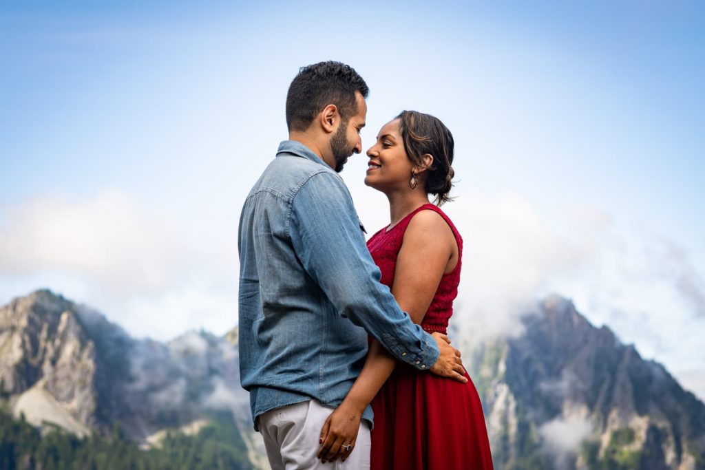 Couple with their arms around each other facing each other with mountains in background