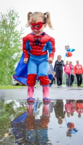 Girl in Spiderman costume with red rain boots is happy to play in the puddle