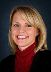 Headshot of a blonde woman with red turtleneck and suit coat
