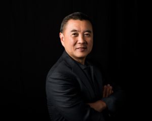 Asian man with arms crossed in front of black backdrop at office in Seattle