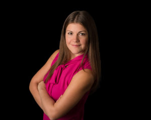 Corporate headshot of a female engineer in pink with black backdrop