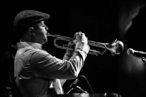 Black and white photo of trumpet player playing with a mute on stage during a jazz concert.