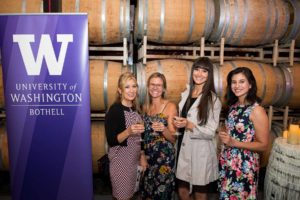 Four women smiling with wine glasses in their hands at a University of Washington event at Columbia Winery in Woodinville