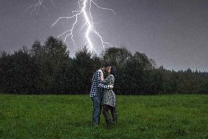 Couple kissing in field with lightning