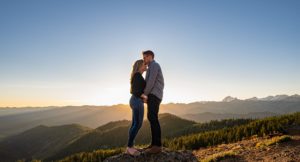 Man kissing woman on forehead at sunset on top of mountain