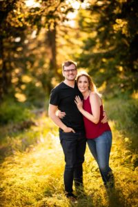 Couple with smiles looks at camera for their engagement photo in a forest
