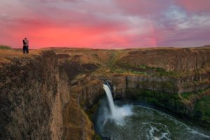Couple looks at each other on top of Palouse Falls at sunset