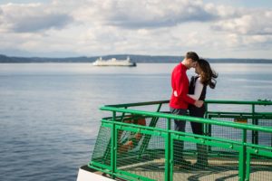Couple on ferry deck holding and facing each other with puget sound in background