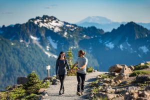Couple holding hands walking on a trail at mt. rainier with mountains in the background
