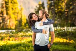 Woman puts arms around fiance in front of wild flowers at Mt. Rainier
