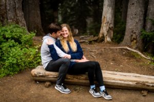 Couple embrace each other while sitting on a log at Mt. Rainier