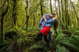 Man dipping his fiancee for a kiss in a mossy forest