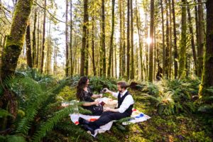 Couple having picnic in forest on blanket and pouring champagne