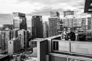 Black and white image of couple holding wine glasses on balcony of their Belltown apartment.