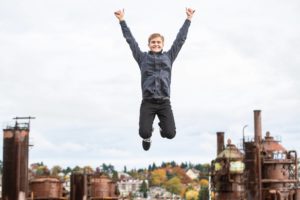 High school senior jumping high with his arms in the air at Gasworks Park in Seattle