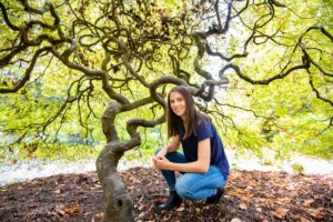 Girl kneeling in front of a Japanese Maple for her senior photos