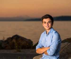 High school senior smiling with arms crossed at sunset with Puget Sound in the background