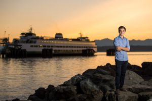Boy crossing his arms at sunset with ferry in background for his senior portraits in Edmonds.