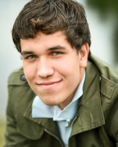 Boy with green jacket on smiling at camera for his senior photos.