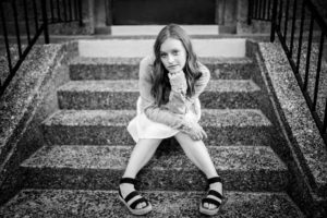 Black and white image of girl sitting on concrete steps and leaning forward with hand under chin