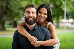 Woman wrapping her arms around her man and both are smiling at the camera.