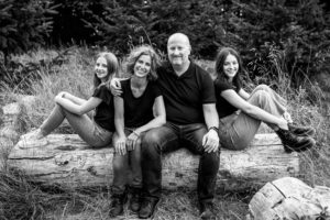 Family sitting on log smiling at camera