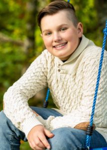 boy wearing white sweater on swing smiling at camera