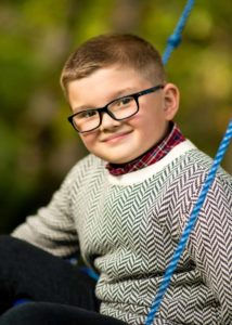 Boy with sweater on swing smiling at camera