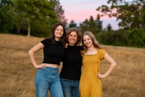 Mother with two teenage daughters in field at sunset