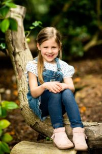 Girl sitting on tree in forest with hands crossed on knee smiling
