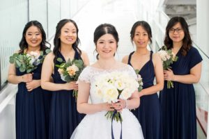 Bride in white dress with bridesmaids in navy blue holding flowers