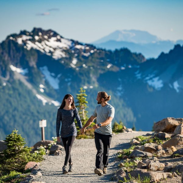 Couple holding hands walking on a trail at mt. rainier with mountains in the background