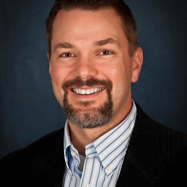 Headshot of a man wearing suit jacket in Seattle with a blue background